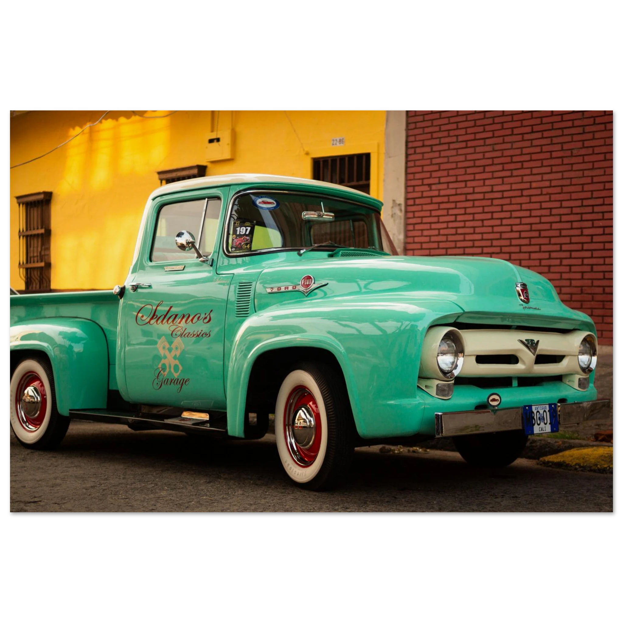 Vintage turquoise truck with white roof parked in front of a yellow building.