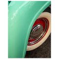 Close-up of a green vehicle's wheel with a red rim and white wall tire.